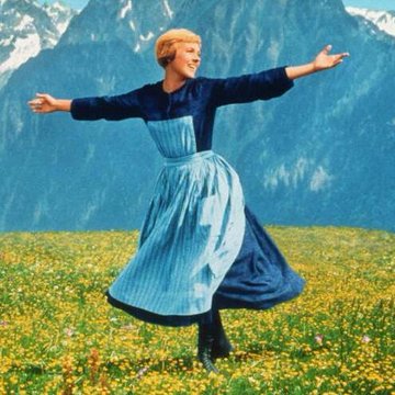 The iconic image of Maria from The Sound of Music, joyfully spinning with arms outstretched in a blue dress and apron against a backdrop of alpine mountains and a flower-filled meadow.