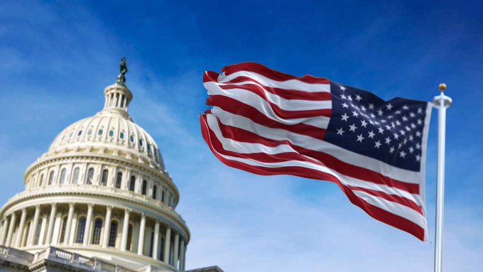 The U.S. Capitol dome stands beneath a waving American flag against a clear blue sky, symbolizing the legislative action referenced in the post about the Senate's 10-day deadline to pass the Crypto Clarity Act before summer recess.