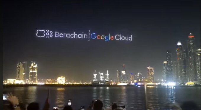 A night view of a city skyline across water, with drones forming the text 'Berachain | Google Cloud' in the sky.