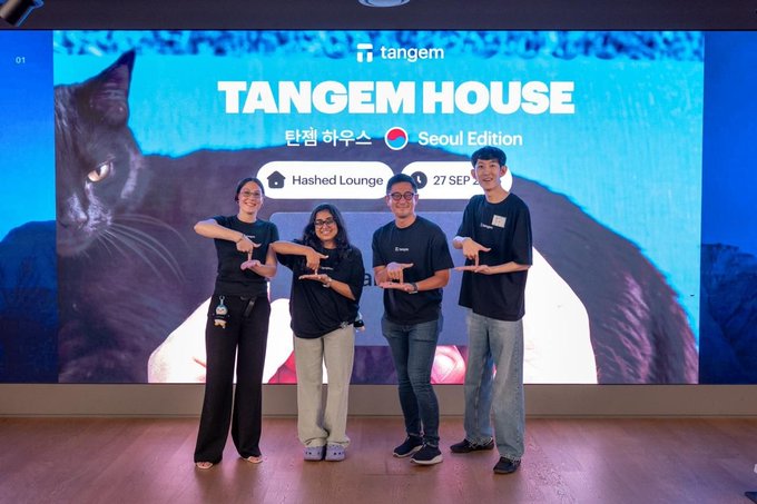 Four people in matching dark t-shirts pose together on a stage in front of a large screen displaying "TANGEM HOUSE," "탕템 하우스 Seoul Edition," "Hashed Lounge," and "27 SEP" alongside a black cat image.