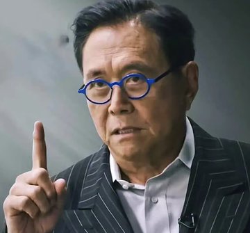 In the image, a man wearing glasses and a suit jacket with blue rimmed glasses is pointing up towards something out of frame while giving an explanation or speech. The caption on the image reads "Robert Kiyosaki said $ETH will hit $1,000,000 this year", indicating that he is talking about a speech given by another individual named Robert Kiyosaki at the International Business Conference in New York City earlier in the year.