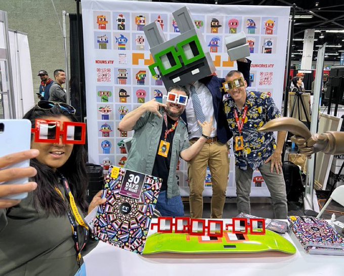 A lively photo from a comic convention or tech event showing people posing with pixelated/blocky 3D-printed character heads and red 3D glasses, with banners reading 'ROBLOX NFT', 'NUNWORKS NFT', and a sign stating '30 DAYS LEFT'.