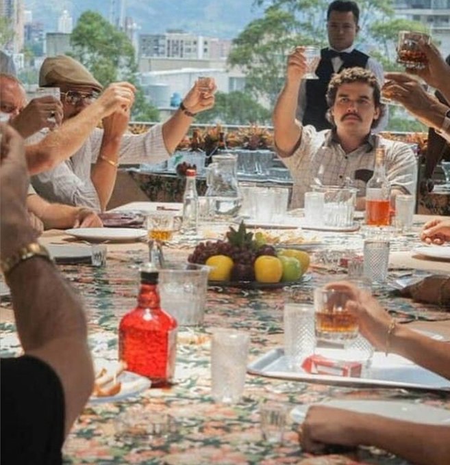 A group of men raise glasses in a celebratory toast at an outdoor banquet table laden with drinks, fruit, and floral linens, with a cityscape visible in the background. The raised glasses and festive atmosphere perfectly capture the spirit of "Cheers to winning the rest of the year," embodying a victorious moment of camaraderie and celebration.