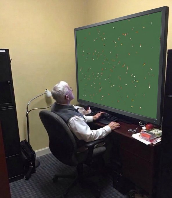 A humorous photo of an elderly man with white hair sitting at a desk using a keyboard, but his monitor is turned to show only the green back of the screen covered in decorative bug-like stickers.