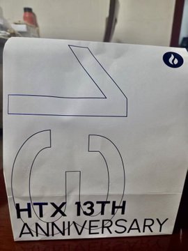 A white paper sign with blue text reading 'HTX 13TH ANNIVERSARY' and a stylized logo, likely displayed in a cafe or store.