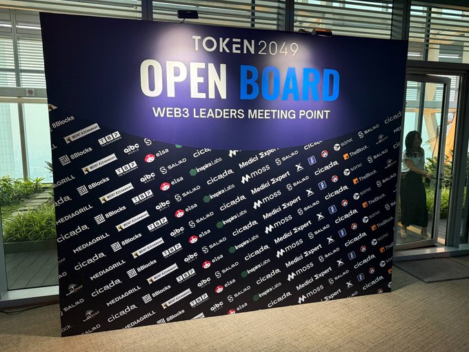 A large display board at TOKEN2049 reading 'OPEN BOARD WEB3 LEADERS MEETING POINT,' surrounded by sponsor logos like cicada, Medli Expert, and SALAD.
