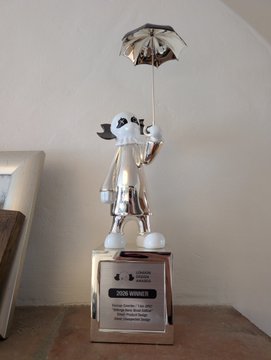 A silver 'JAKE WHITNEY AWARD' trophy featuring a cartoon character holding an umbrella, displayed in a glass case.