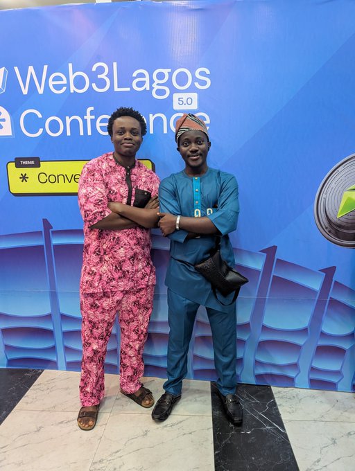 Two young men pose confidently with arms crossed in front of a "Web3Lagos Conference 5.0" backdrop, which also displays the theme "Convergence." One wears a vibrant pink patterned traditional outfit while the other sports a teal ensemble with a matching cap, capturing the celebratory close of Day 2 before heading to the mixer with the Web3Unilag crew.