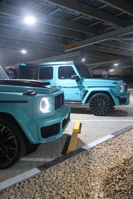 Two custom turquoise Mercedes-Benz G-Wagons are parked side by side in a covered garage, their bold paint job and aggressive styling standing out under the overhead lights. The "GN" caption likely refers to a garage or car collection associated with those initials, possibly showcasing these matching luxury SUVs as part of a curated fleet.