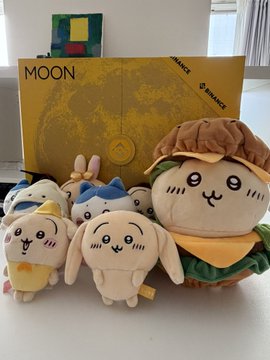 A collection of Chiikawa plush toys displayed in front of a yellow 'MOON' themed box, featuring characters in burger-themed outfits.