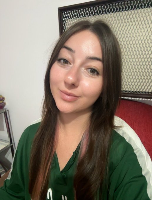 A selfie of a young woman with long brown hair wearing a green and white button-up jersey-style shirt.