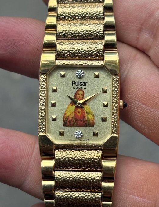 A hand holds a gold Pulsar Quartz watch featuring an unusual face decorated with an image of the Virgin Mary and two diamond-shaped gems at the top and bottom.