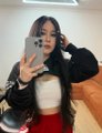 A mirror selfie of a person wearing a black jacket and white top, holding a phone to take the photo.