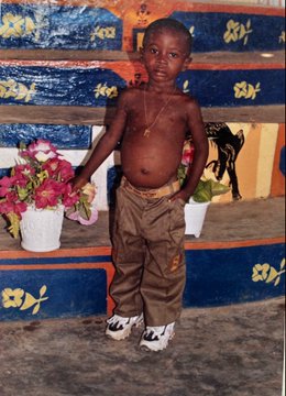 A shirtless young boy stands between two potted plants with pink and yellow flowers, wearing brown cargo pants and white sneakers, in front of a wall decorated with blue, orange, and white painted patterns. The image's context of depicting poverty-stricken children aligns with the post's critique of crypto rug pulls, implying that fraudulent token creators harm vulnerable communities in developing regions.