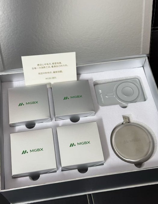 An unboxed MGBX hardware wallet set displaying four silver product boxes, a metallic card device, and a round charging accessory, with a note in Chinese mentioning 'MGBX 团队' (MGBX team).
