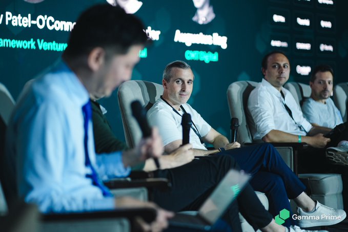 Panelists sit in chairs at a conference, with on-screen text showing names including 'Augustus Ring' and 'Patel-O'Connor', and a 'Gemma Prime' watermark.