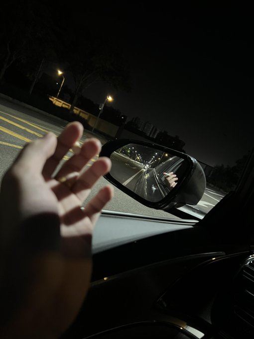 A hand reaches out toward a side mirror on a nighttime drive, reflecting streetlights and the open road behind. The image mirrors the post's reflection on life's path—when the road ahead feels blocked, we start watching every sign and signal, searching for any move that might change direction.