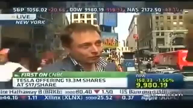 The image shows a news broadcast of a man talking about Tesla, Apple, and shares with a city street view as part of his presentation. The text "First On Cbc" suggests that this is an advertisement or segment from a cable network. The image also includes a caption that reads "If you're having a bad day Remember someone sold their kidney in 2022 to buy a Bored Ape". This caption seems unrelated to the main content of the news broadcast, but it could be interpreted as a reminder for viewers to consider the impact of their actions on others.