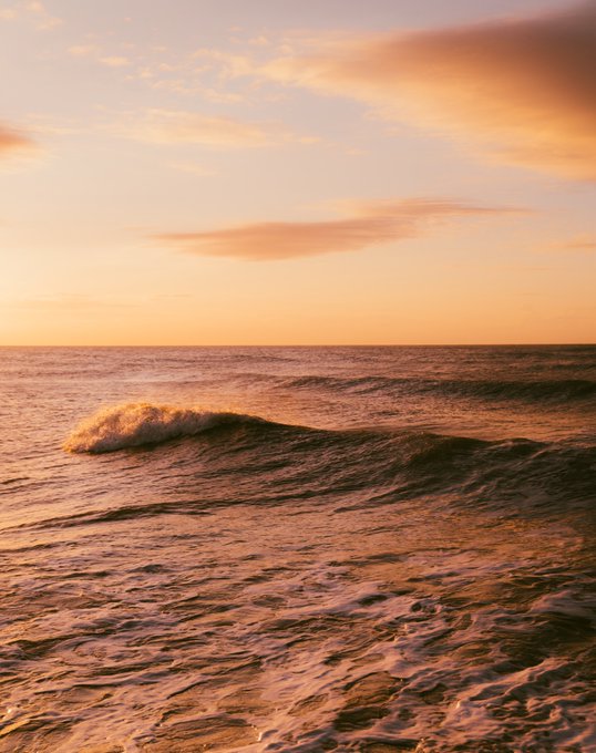 A scenic photograph of ocean waves rolling under a soft orange and peach-colored sky, suggesting sunset or sunrise.