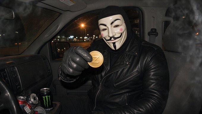 A person wearing a Guy Fawkes mask and black leather jacket sitting in a vehicle, holding up a gold 'Z' cryptocurrency coin, with a Monster Energy can visible on the dashboard.