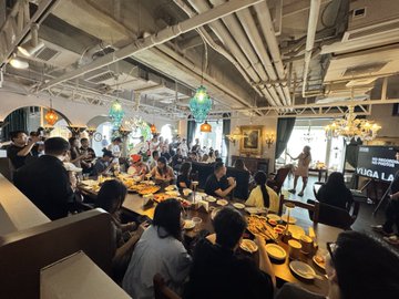 A lively gathering of Bored Ape community members enjoying dinner together at a bustling restaurant, with a "KUSA LA" sign visible in the background, capturing the social atmosphere of the Shanghai meetup described in the post. The packed room reflects the large turnout of "apes" the poster mentioned not being able to speak with individually.