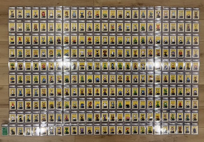 A large collection of small character figures, appearing to be LEGO minifigures or similar collectibles, arranged in a dense grid on a wooden surface.