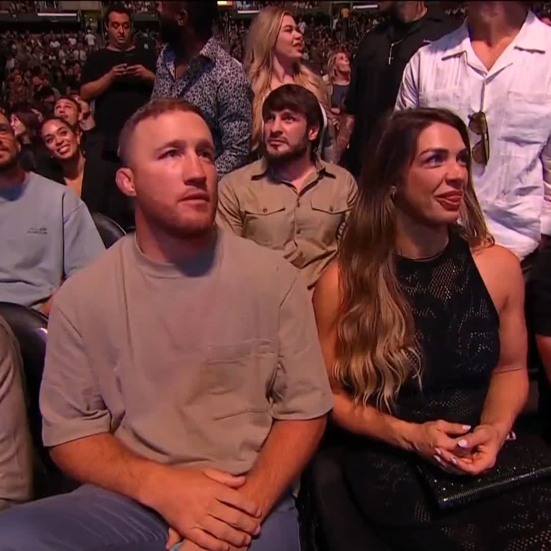 Justin Gaethje and Mackenzie Dern sit together ringside at UFC 331, watching the action unfold at what appears to be a sold-out arena event. Their attentive expressions match the post's "Champions unite" caption, highlighting the gathering of top MMA fighters in attendance.