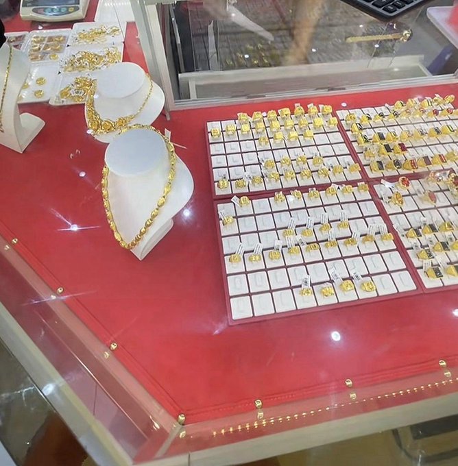 A display case in a gold jewelry shop showcases an extensive collection of gold rings, necklaces, and earrings arranged on red velvet trays, reflecting the post's message about how life changes dramatically with wealth—from looking "haggard like a ghost" when broke to feeling like royalty when flush with money.