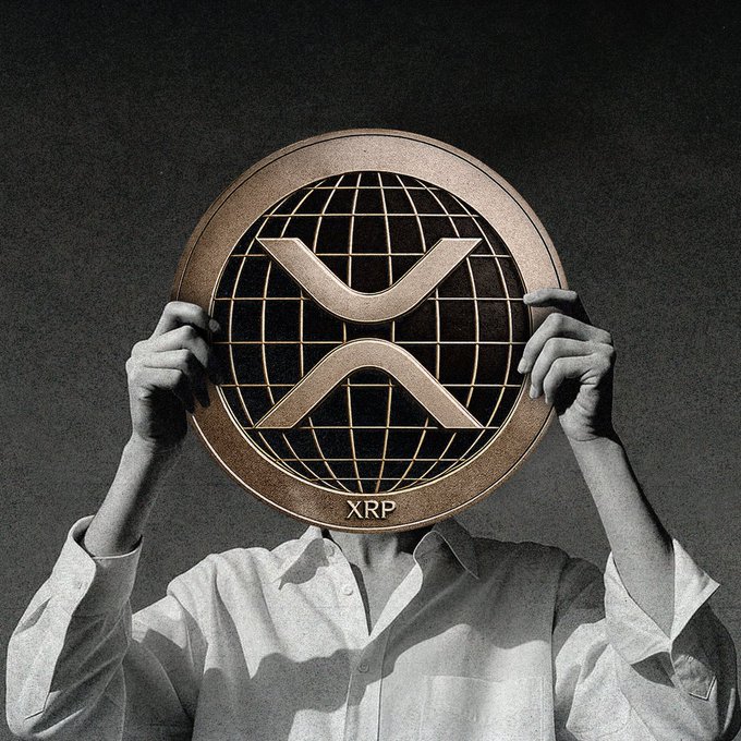 A person in a white shirt holding a large bronze XRP (XRP cryptocurrency) coin in front of their face against a dark background.