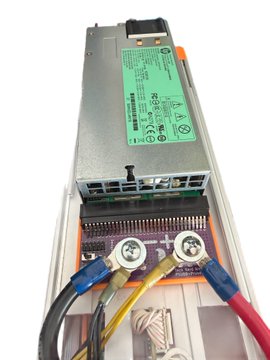Close-up of a power supply unit with a green label mounted in a chassis, with blue, yellow, and red power cables connected to a small PCB.