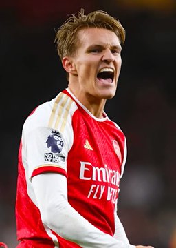 Martin Ødegaard, Arsenal captain wearing the team's iconic red and white kit with the "Emirates Fly Better" sponsor and Premier League badge, celebrates passionately during a match, likely in the context of the Arsenal vs Manchester City Community Shield game referenced in the betting payout announcement.