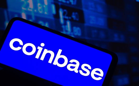 A smartphone displays the Coinbase logo against a backdrop of blue stock tickers and numbers, visually tying to the post about Coinbase's $150,000 FOIA settlement with the SEC, following its earlier $188,440 win from the FDIC. The financial data screen reinforces the legal and regulatory focus of the news.