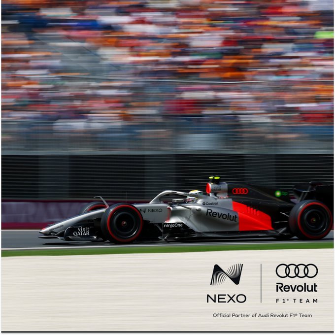 A promotional image for NEXO as the Official Partner of the Audi Revolut F1 Team, showing a Formula 1 race car in motion on a track with motion-blurred spectators in the background.