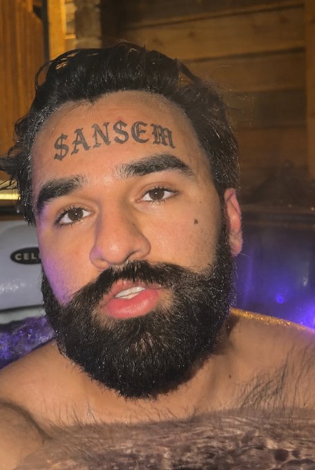 A bearded man relaxes in what appears to be a hot tub or jacuzzi, with the word "ANSEM" tattooed across his forehead. The image ties into the post's request to feature @blknoiz06, referencing the $ANSEM ticker mentioned.