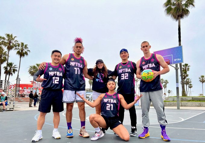A team of six players poses together on an outdoor basketball court, wearing matching black and pink "NFTBA" jerseys with visible numbers including 11, 12, 21, and 32, while one player holds a colorful basketball—fitting the post's boast that "Team Kiki" dominated the NFTBA competition.