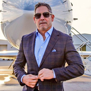 Grant Cardone, dressed in a blue plaid blazer and sunglasses, buttoning his jacket while standing in front of a private jet on a tarmac—visually reinforcing his caption about Bitcoin and his plane.