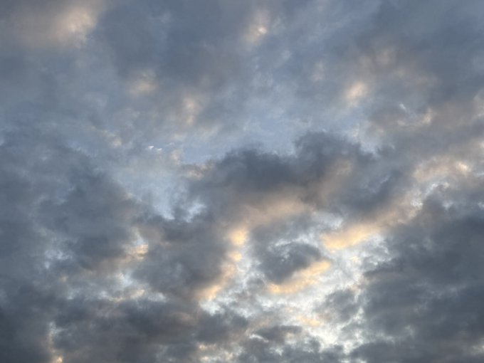 A sky filled with scattered clouds illuminated by soft sunlight, with subtle hues of blue, gray, and pale orange.