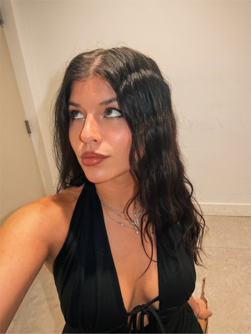 A selfie of a young woman with long dark wavy hair wearing a black halter top and silver necklaces.
