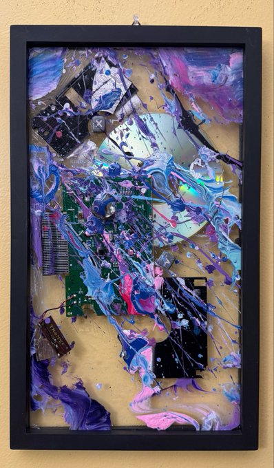 A framed piece of mixed-media artwork incorporating electronic components like a CD, circuit board, and chips, heavily splattered with swirling purple, pink, blue, and white paint.