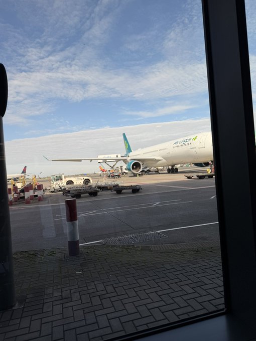 A view through an airport window showing a Bamboo Airways airplane parked on the tarmac with ground vehicles nearby.