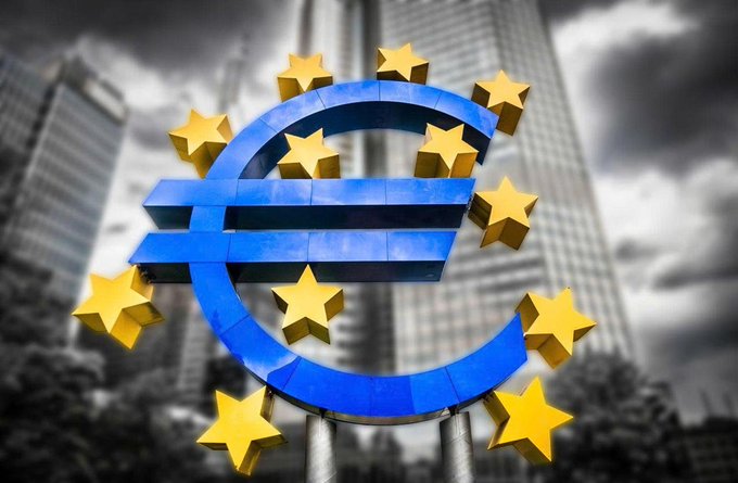 A 3D illustration of a blue Euro (€) symbol surrounded by gold stars, set against a backdrop of European government buildings and a cloudy sky.