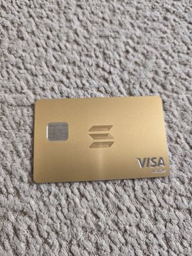 A gold metallic Visa credit card with a chip resting on a gray textured carpet.
