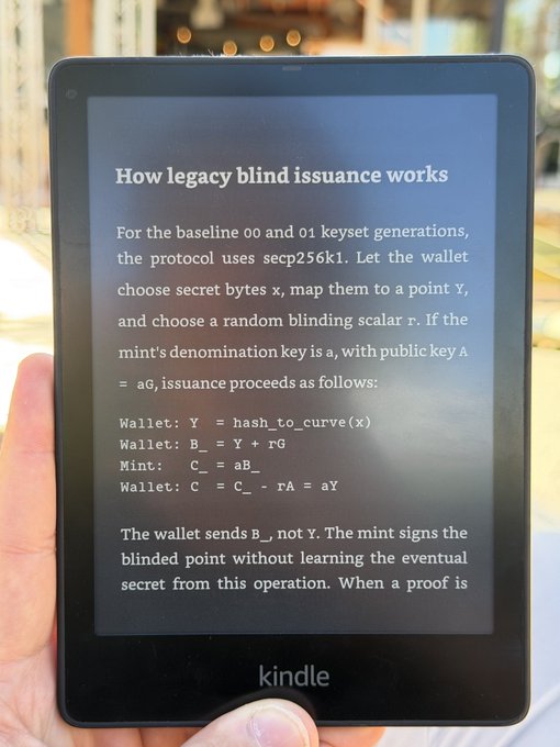 A hand holds a black Kindle e-reader displaying a technical text titled 'How legacy blind issuance works' which explains cryptographic protocols using secp256k1, including equations like 'Wallet: Y = hash_to_curve(x)' and 'Mint: C_ = aB_'.