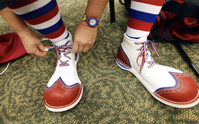 Close-up of a person wearing red, white, and blue striped socks and distinctive white and red bowling-style shoes, tying the laces, with a cartoon face watch on the wrist.