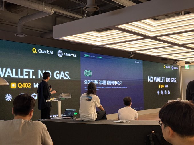 A conference or presentation room where attendees are gathered in front of a large screen displaying 'NO WALLET. NO GAS.' with 'Quack AI' and 'MANTLE' logos, alongside Korean text.