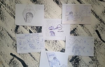 Several small hand-drawn storyboard or comic sketches on lined paper scattered on a patterned black and white rug, with the word "DELTA" visible on one.