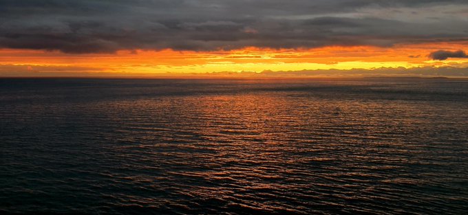 A dramatic ocean sunset with dark storm clouds above and bright orange light reflecting off the rippling water below.
