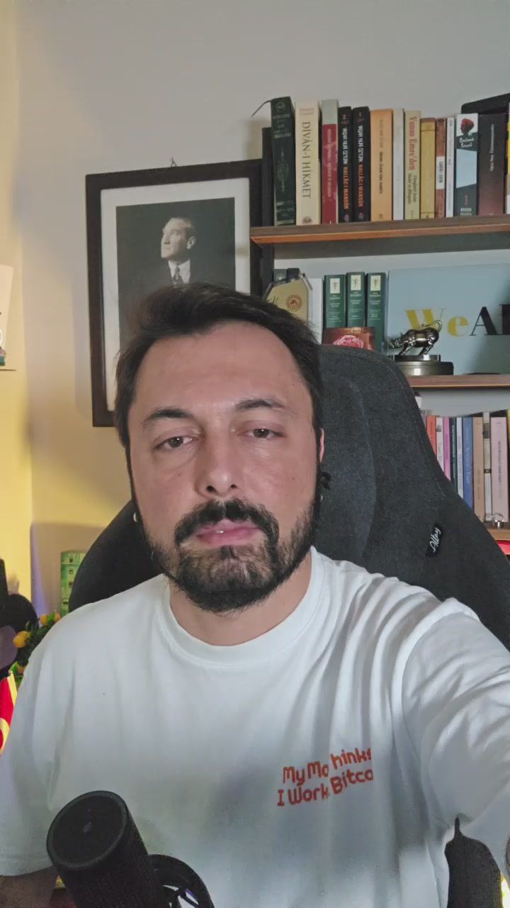 The image features a man wearing a white t-shirt with an orange message that reads "I'm not interested" written on it. He is sitting in front of a bookshelf filled with various books, suggesting he might be reading or studying. The background includes a wall and a picture hanging above the bookshelf.