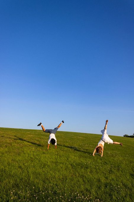 Two people do handstands on a grassy hill under a clear blue sky, perfectly capturing the "Me after Agent OS:" feeling of being flipped upside down by a powerful experience.
