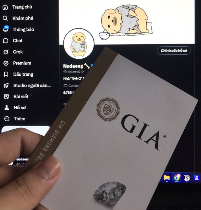 A hand holding a GIA diamond certificate box in front of a computer screen displaying a Twitter/X profile page.